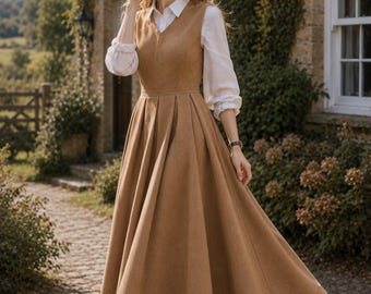 May include: A tan sleeveless V-neck dress with a fitted bodice and a pleated, floor-length skirt, worn over a white long-sleeved collared shirt with cuffed sleeves, paired with dark brown leather ankle boots with a block heel.