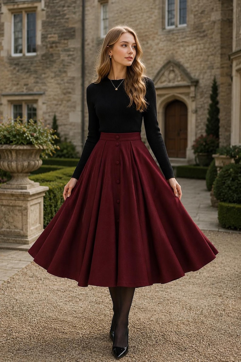 May include: A long-sleeved black ribbed jumper paired with a high-waisted, calf-length burgundy skirt. The skirt features a central vertical row of matching buttons, a structured waistband, and a full, pleated silhouette that flares outward.