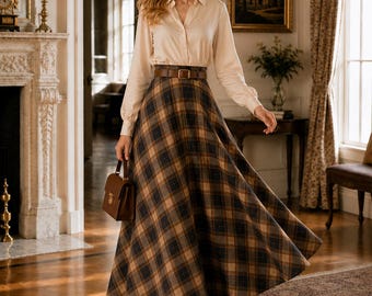 May include: A long-sleeved beige button-down shirt paired with a high-waisted, floor-length plaid skirt in shades of brown, black, and tan. The outfit includes a brown leather belt with a gold buckle and a small brown structured handbag.