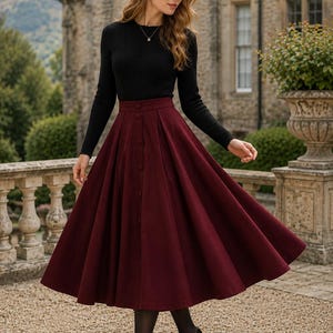 May include: A long-sleeved black ribbed jumper paired with a high-waisted, pleated burgundy midi skirt. The skirt features a vertical row of matching buttons down the centre front, creating a structured, flared silhouette that falls below the knees.