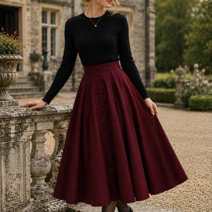 May include: A long-sleeved black ribbed jumper with a crew neckline paired with a high-waisted, calf-length burgundy skirt. The skirt features a vertical row of matching fabric buttons down the centre front and a full, pleated silhouette.