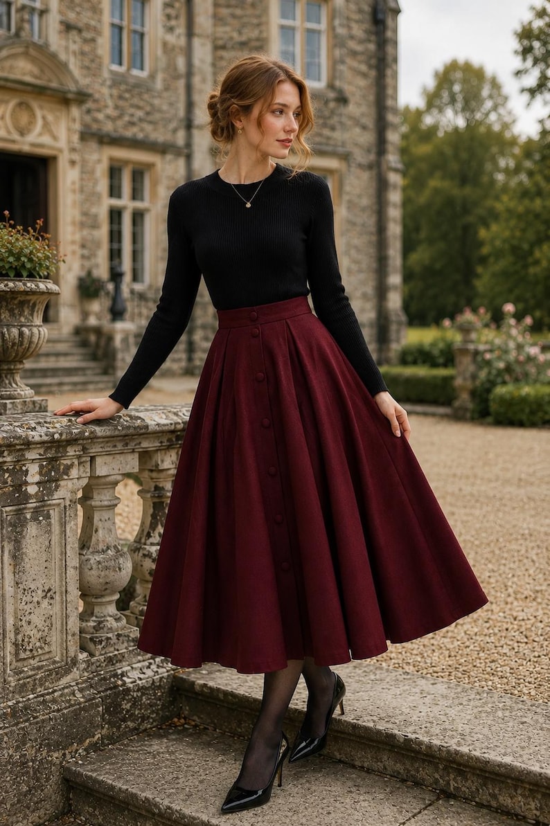 May include: A long-sleeved black ribbed jumper with a crew neckline paired with a high-waisted, calf-length burgundy skirt. The skirt features a vertical row of matching fabric buttons down the centre front and a full, pleated silhouette.