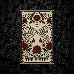 May include: A rectangular cross-stitch embroidery featuring two skeletal hands performing a pinky promise. The design is framed by black scrollwork and red roses with green leaves on a cream background, with the text THE SISTER at the bottom.