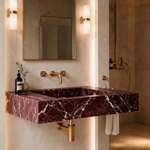 Puede incluir: Un lavabo de pared fabricado en mármol rojo intenso con vetas blancas prominentes. El lavabo cuenta con un grifo de oro cepillado y accesorios de fontanería a juego, complementado por un espejo rectangular y dos apliques de pared cilíndricos.
