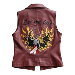 May include: A maroon sleeveless vest featuring a large embroidered graphic on the back. The design depicts a figure with long blonde hair holding a spear, surrounded by black and yellow flames. The text Let me live is embroidered above.