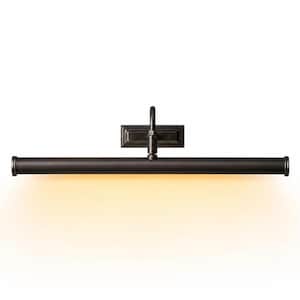 May include: A dark bronze picture light fixture featuring a long, horizontal cylindrical lamp head attached to a rectangular wall-mounting plate by a central arm. The fixture emits a warm, soft yellow glow downward from the underside of the tube.