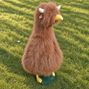 May include: A plush duck figurine covered in long, shaggy brown faux fur. The duck features a smooth, solid yellow beak, two small white horns protruding from the top of its head, and bright yellow webbed feet attached to a dark green base.