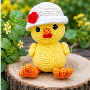 Könnte beinhalten: Eine gelbe, gehäkelte Kükenfigur mit einem weißen Hut, der mit einer kleinen roten Blume verziert ist. Das Küken hat schwarze Perlenaugen, einen orangefarbenen Schnabel und orangefarbene Füße. Die Textur besteht aus Garn mit sichtbaren Maschen.