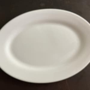 May include: A plain white oval serving platter with a smooth, glossy finish and a slightly raised rim. The dish features a simple, clean design with no patterns, textures, or decorative elements, presenting a solid white color throughout.