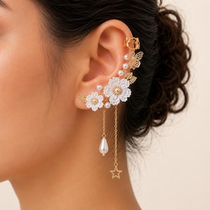 May include: A gold-toned ear cuff featuring white floral lace accents, small white faux pearls, a delicate butterfly charm, and two dangling gold chains. One chain ends in a white teardrop-shaped faux pearl, while the other features a small gold star.