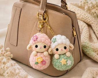 May include: Two crocheted sheep keychains attached to a gold-toned metal ring. One sheep is pink with a pink flower on its head and yellow and pink flowers on its body. The other sheep is white with a green star on its head and yellow and white stars.
