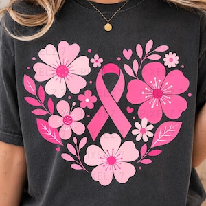 Op de afbeelding: Een antracietgrijs t-shirt met korte mouwen en een grote hartvormige afbeelding bestaande uit roze bloemen, bladeren en een roze bewustzijnslint in het midden. Het ontwerp is gecentreerd op de borst en toont diverse bloemvormen.