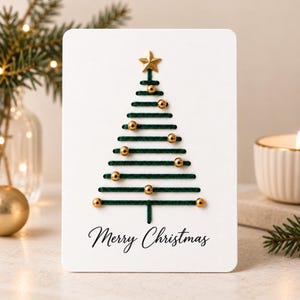 May include: A white rectangular greeting card featuring a stylized Christmas tree created with dark green thread stitched in horizontal lines. The tree is decorated with small gold metallic beads and topped with a gold star. The text Merry Christmas is printed in black script at the bottom.