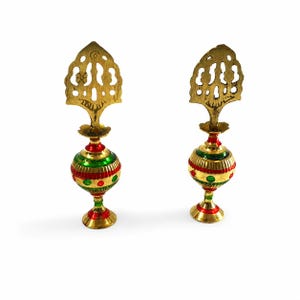 May include: Two matching metal perfume bottles featuring a rounded body with alternating red and green horizontal stripes and circular accents. Each bottle is topped with an ornate, flat, gold-toned metal stopper with cut-out detailing.