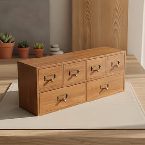 Könnte beinhalten: Ein rechteckiger Schreibtisch-Organizer aus Holz mit sechs Schubladen in unterschiedlichen Größen. Jede Schublade ist mit einem kleinen messingfarbenen Metallgriff und einem rechteckigen Etikettenhalter ausgestattet.