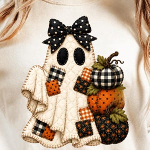 Könnte beinhalten: Ein cremefarbenes Sweatshirt mit einer gesteppten Geistergrafik. Der Geist trägt eine schwarz-weiß gepunktete Schleife, hat schwarze ovale Augen und ist mit verschiedenen Stoffflicken in Karomustern und Blumenmustern verziert. Er hält drei Kürbisse.