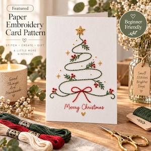 May include: A white paper embroidery card featuring a stitched green Christmas tree design with red berries, a red bow at the base, and a gold star at the top. The text Merry Christmas is stitched in red below the tree with a small gold heart.
