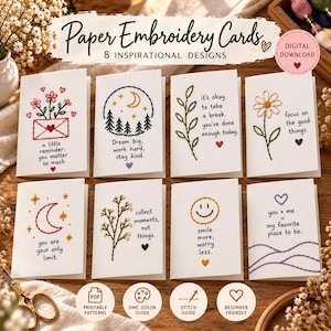 Puede incluir: Ocho tarjetas de bordado en papel blanco con diseños y texto cosidos. Los patrones incluyen flores, un bosque a la luz de la luna, una margarita, una luna creciente, una ramita, una cara sonriente y corazones con frases motivadoras.