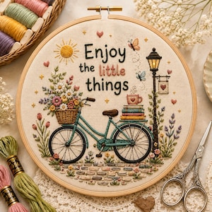 Puede incluir: Un bastidor de bordado circular con una bicicleta color verde azulado con una cesta de flores, una pila de libros, una taza y una farola sobre tela crema. El texto dice Enjoy the little things, rodeado de sol, corazones y estrellas.