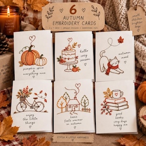 Puede incluir: Un juego de seis tarjetas de felicitación blancas con diseños bordados de temática otoñal que incluyen una calabaza, un pastel, un gato, una bicicleta, una casa y libros. Cada tarjeta incluye texto y corazones bordados, indicando 5 x 7 pulgadas.