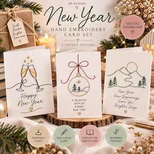 Op de afbeelding: Een set van drie witte wenskaarten met handgeborduurde ontwerpen voor het nieuwe jaar. De kaarten tonen illustraties van champagneglazen, een hangende kerstbal en een berglandschap met teksten zoals Happy New Year en New Beginnings.
