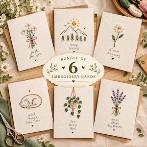 Op de afbeelding: Een set van zes off-white wenskaarten met handgeborduurde ontwerpen, waaronder madeliefjes, bergen, een slapende kat, een hangplant en lavendel. Elke kaart bevat een unieke tekst zoals 'just for you' en 'Keep Going'.