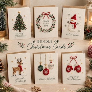 Peut inclure: Un lot de six cartes de vœux blanc cassé avec des motifs de Noël brodés : un sapin, une couronne avec le texte Peace Love Joy, un bonhomme de neige avec Let it Snow, un renne avec Season's Greetings, des boules avec Warm Wishes et des moufles avec Stay Cozy This Christmas.