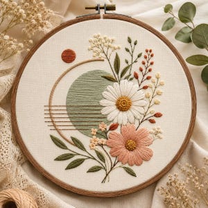 May include: A circular wooden embroidery hoop containing a fabric panel with hand-stitched floral designs. The embroidery features a large white daisy, a pink flower, green leaves, and a sage green circular shape with horizontal brown lines.