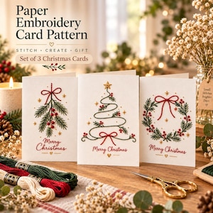 May include: A set of three white paper embroidery cards featuring stitched Christmas designs of a mistletoe, a tree, and a wreath. Each card displays the text Merry Christmas in red thread. Includes embroidery floss and gold scissors.