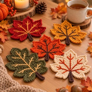 May include: A set of five crocheted leaf coasters in autumn colors including red, orange, yellow, green, and cream. Each coaster features a detailed stitched vein pattern and a small stem, arranged on a wooden surface with seasonal decor.