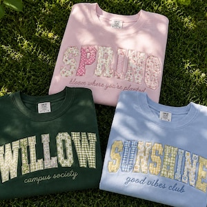 May include: Three crewneck sweatshirts in light pink, dark green, and light blue. The pink sweatshirt features the text SPRING and bloom where you're planted. The green one says WILLOW campus society. The blue one says SUNSHINE good vibes club.