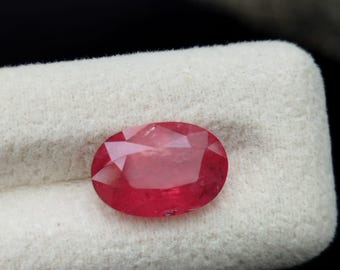 Op de afbeelding: Een levendige, ovaal geslepen edelsteen met een dieprode tint en een gefacetteerd oppervlak. De steen heeft een gepolijste afwerking die het licht reflecteert over de symmetrische, afgeronde randen, wat een heldere, transparante kwaliteit toont.
