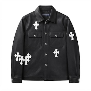 Puede incluir: Una chaqueta negra de manga larga con cuello en punta, cierre frontal de botones y dos bolsillos en el pecho. La chaqueta está decorada con varios parches blancos en forma de cruz en la parte delantera y las mangas. Una etiqueta azul es visible en el cuello.