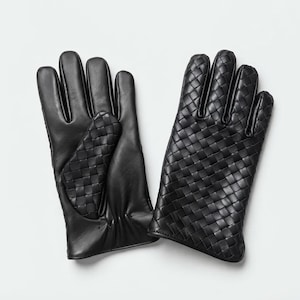 Könnte beinhalten: Ein Paar schwarze Handschuhe. Ein Handschuh hat eine glatte Lederhandfläche mit einem geflochtenen Lederaufnäher an der Fingerbasis. Der andere Handschuh ist auf dem Handrücken und den Fingern vollständig mit einem Flechtmuster versehen.