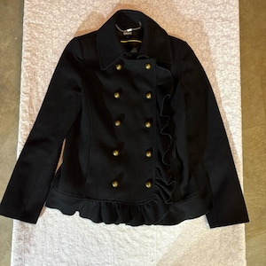 May include: A black double-breasted jacket featuring a structured collar, long sleeves, and eight metallic gold-toned buttons arranged in two vertical rows. The front panel is accented with a vertical ruffle detail and a ruffled hemline.
