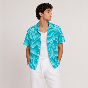 Op de afbeelding: Een overhemd met korte mouwen en knoopsluiting, voorzien van een levendig turquoise en lichtblauw wervelpatroon. Het overhemd heeft een klassieke kraag en wordt gedragen over een effen wit hemd, gecombineerd met een witte broek met trekkoord.