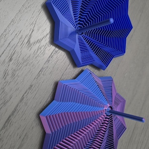 May include: Two star-shaped, multi-layered geometric objects with a central rod. The top object is solid blue, while the bottom object features a gradient transition from blue to purple. Both items have a stepped, concentric design.