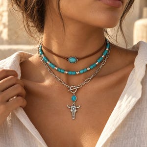 Peut inclure: Un ensemble de colliers superposés composé d'un ras-de-cou en cordon marron avec une pierre turquoise centrale, d'un rang de perles turquoise et argent, et d'une chaîne argentée avec fermoir à bascule, pierre turquoise et pendentif crâne de taureau.