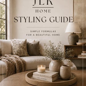 Könnte beinhalten: Ein digitaler Ratgeber mit dem Titel JLK HOME STYLING GUIDE SIMPLE FORMULAS FOR A BEAUTIFUL HOME. Das Cover zeigt ein Wohnzimmer mit beigem Sofa, gemusterten Kissen, einem hölzernen Couchtisch mit rundem Tablett, zwei Büchern, einer Kerze und Vasen.