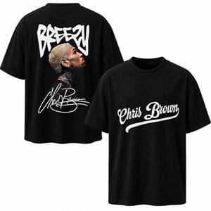 May include: A black short-sleeved t-shirt featuring a white graphic on the front that reads Chris Brown in cursive script. The back displays a photographic portrait of a person with blonde hair, the word BREEZY in white, and a white signature.