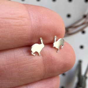 May include: A pair of silver rabbit silhouette stud earrings. The earrings are small and delicate, and they are perfect for adding a touch of whimsy to any outfit.
