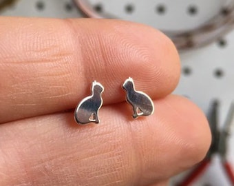Peut inclure: Une paire de boucles d'oreilles en argent en forme de chat. Les boucles d'oreilles sont petites et délicates, et elles présentent une silhouette de chat simple.