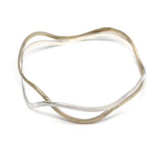Puede incluir: Un brazalete de plata y oro con un diseño ondulado.