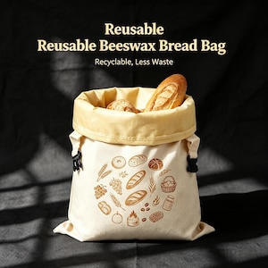 May include: A reusable beeswax bread bag with a cream-colored exterior featuring brown illustrations of bread, wheat, and jars. The bag has a yellow interior lining, black side buckles, and contains two loaves of bread. Text reads: Reusable Beeswax Bread Bag, Recyclable, Less Waste.
