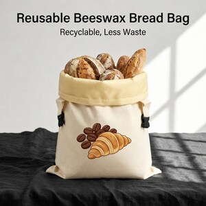 May include: A cream-colored reusable beeswax bread bag with a rolled top, filled with various crusty loaves of bread. The bag features a graphic print of a croissant and coffee beans, with the text Reusable Beeswax Bread Bag, Recyclable, Less Waste.