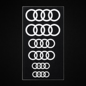 May include: A rectangular sheet of clear adhesive material featuring six white vinyl decals of the four-ring logo, arranged in a vertical column from largest to smallest. Each decal consists of four interlocking circles in a horizontal row.