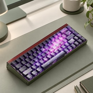 May include: A compact mechanical keyboard with a dark olive green frame and a translucent red top accent bar. The keys feature a deep purple and black nebula-inspired pattern with white lettering, illuminated by a vibrant purple backlight.