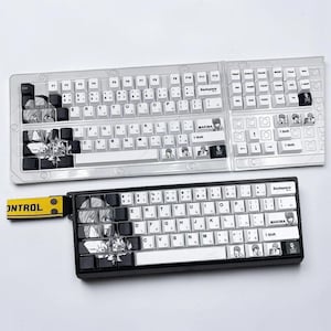 May include: A mechanical keyboard with white and black keycaps featuring anime-style character illustrations and the text "MAKIMA" and "CONTROL" on a yellow fabric tag. The keyboard has a standard layout with alphanumeric keys and symbols.
