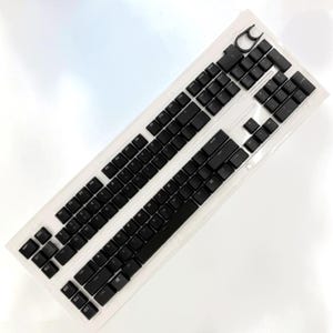 May include: A mechanical keyboard featuring a white frame and black keycaps. The layout includes a standard QWERTY arrangement with a dedicated number pad, function keys, and a circular volume knob located in the upper right corner of the device.