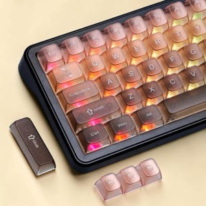 May include: A mechanical keyboard featuring translucent brown keycaps with white lettering and integrated RGB lighting. The keyboard includes a black frame, with an additional loose shift key and three function keys labeled F4, F5, and F6 nearby.
